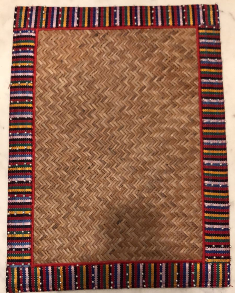 A red placemat with a geometric pattern, featuring a natural brown center and a colorful striped border.